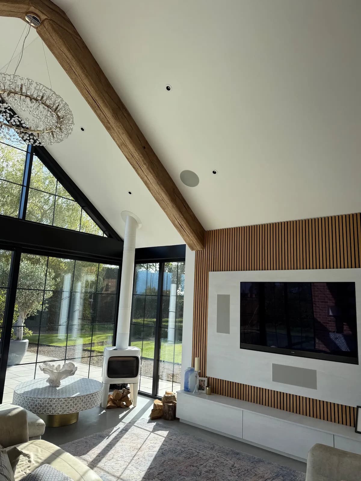 Chandelier and media wall in a vaulted room, with a wall-mounted TV and speaker on oak slats