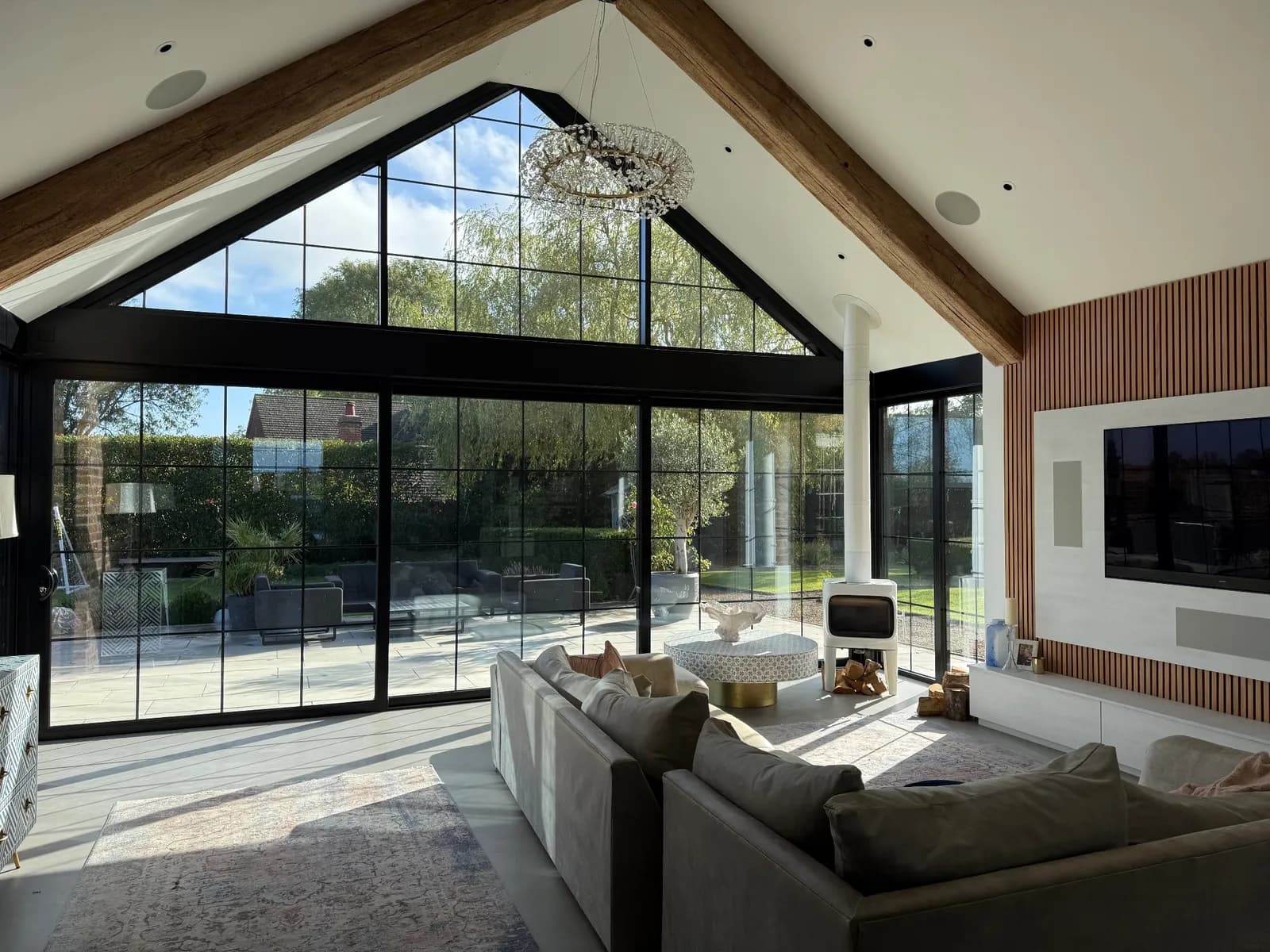 Designer lighting in a vaulted living room, with a crystal chandelier, ceiling speakers and a glazed gable wall